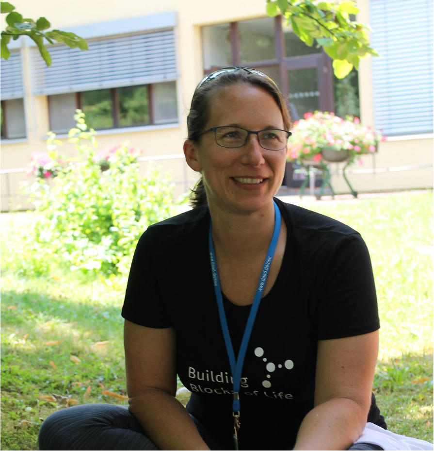Picture of a woman wearing glasses seated in the grass outside on a sunny day.